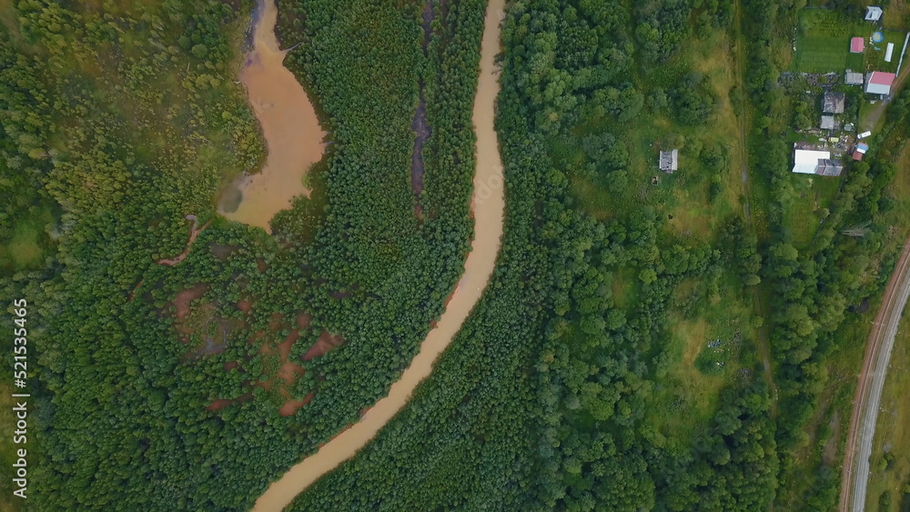 A huge dirty river in the forest. The view from the drone. Clip. A huge curving dirty river with petroleum products that flows next to a huge green forest and several small houses for people are