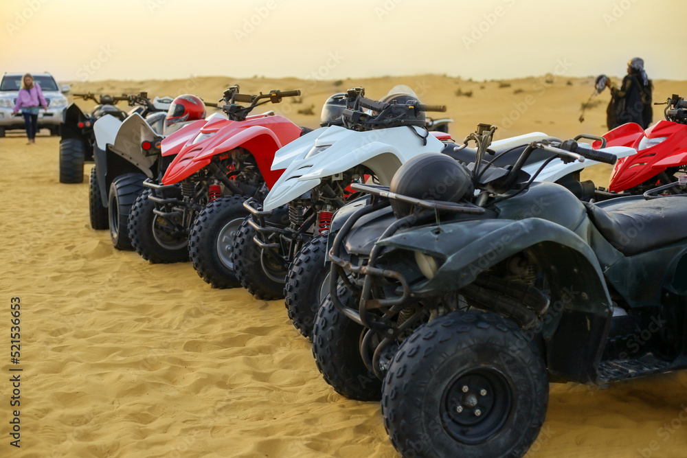 Line of ATVs stand in orange desert sand