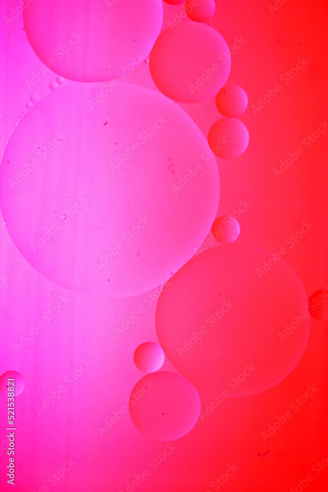 Burbujas difuminadas de color rojo y violeta flotando en el lìquido de agua y aceite con jabòn, producen esferas grandes y pequeñas formando un bello y original diseño abstracto en bokeh