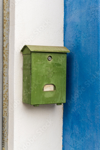 Old green mailbox on the white and blue wall of the house