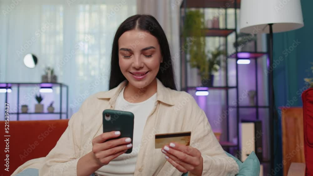 Lovely girl using credit bank card and smartphone while transferring money, purchases online shopping, order food delivery at modern home apartment indoors. Young woman in living room lying on couch Lovely girl using credit bank card and smartphone while transferring money, purchases online shopping, order food delivery at modern home apartment indoors. Young woman in living room lying on couch