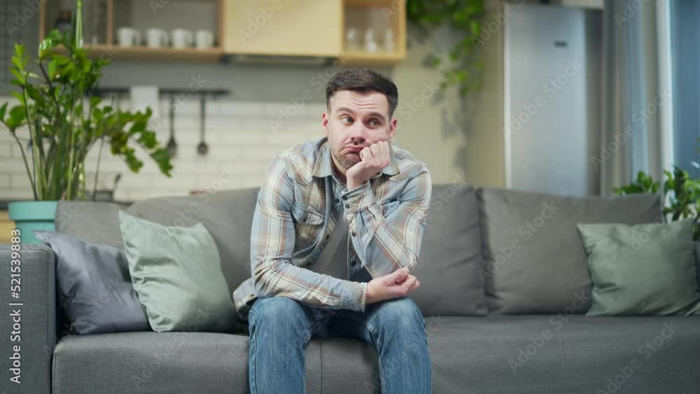 Portrait Bored exhausted sad young man bearded handsome man sitting alone on the sofa at home in the living room. Waiting thought male holding his head with hand lonely melancholy and depression Portrait Bored exhausted sad young man bearded handsome man sitting alone on the sofa at home in the living room. Waiting thought male holding his head with hand lonely melancholy and depression