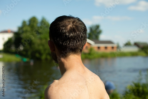 Guy without T-shirt with bare back on beach. Man is on vacation in summer. Guy sunbathes in sun.