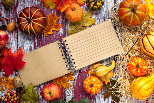 Pumpkins and autumn leaves on the table and a notebook with an open page for text.