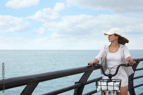Beautiful young woman with bicycle near sea. Space for text