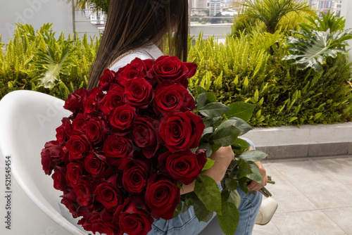 woman sitting on her back holding a large bouquet of red natural roses on a terrace, lifestyle and beauty of nature in the day, romantic gift