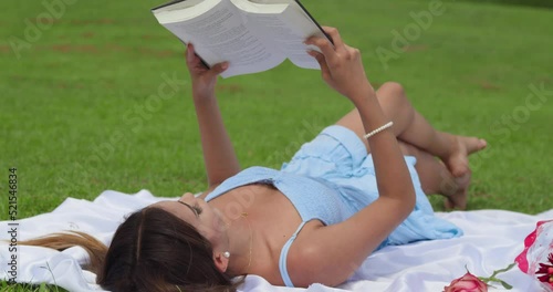 Young latina girl enjoys reading a book while laying in the park at a picnic setting photo