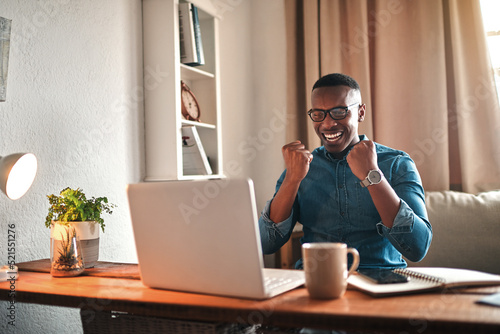 Businessman reading good news on a laptop, looking excited and happy after a loan approval, winning a reward or an online sale while at home. Excited freelance worker with a cheerful expression