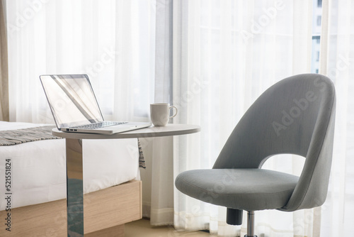 laptop and coffee cup on table and chair in bedroom