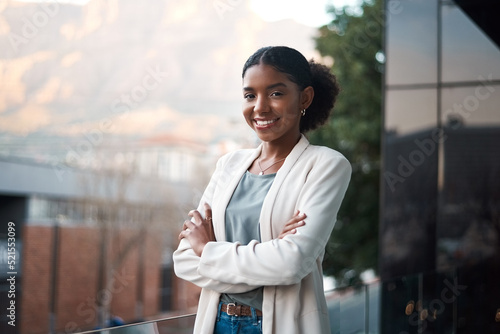 Confident business woman with arms crossed standing outside of an office at work. Portrait of one happy, smiling and expert corporate professional with arms folded working at a startup company photo