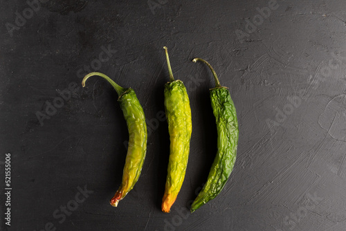 Fotografie tres chiles serranos o chile verde sobre base de madera negra en proceso de seca