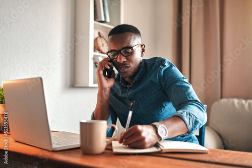 Foto Young serious professional businessman talking on phone call, writing and sitting with digital laptop at home office