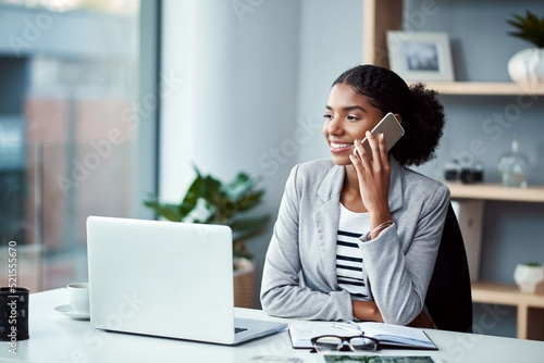 Business woman talking on phone call or young entrepreneur answering cellphone in front of laptop in work office. Happy, African American female smiling and receiving good news while sitting at desk.