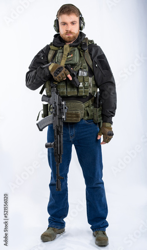 airsoft player in full gear with weapons series GG RK74 fire. a man in an outfit, in headphones, a bulletproof vest, with a backpack and a belt. White background.