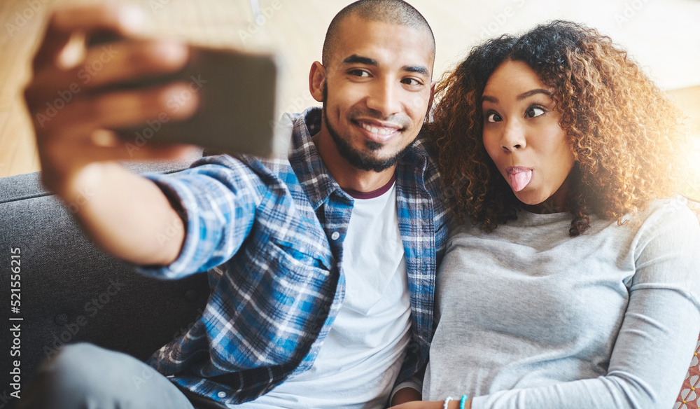 Obraz premium Funny and silly couple taking selfie and making goofy face at phone for social media post while relaxing. Boyfriend and girlfriend having fun and enjoying time together at home and sharing it online
