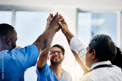 Doctors celebrating medical success after working together as a team and give each other motivating a high five as a group in a hospital. Healthcare workers joining hands in a huddle showing teamwork