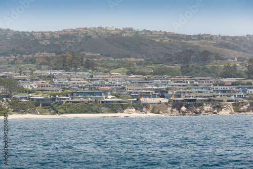 A view of the Newport Beach coastline, with large mansion homes on hillsides and cliffs, in the background.