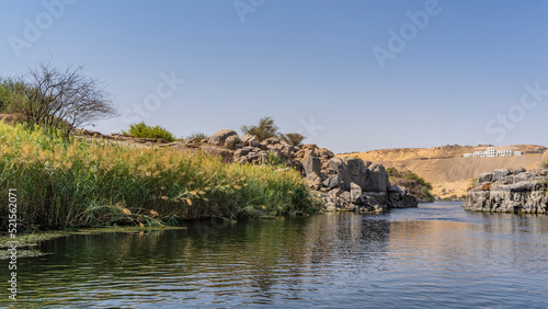 A quiet backwater in the riverbed. There are thickets of reeds near the shore, duckweed on the water. Picturesque boulders and a sand dune against a clear blue sky. Egypt. Nile. Aswan photo