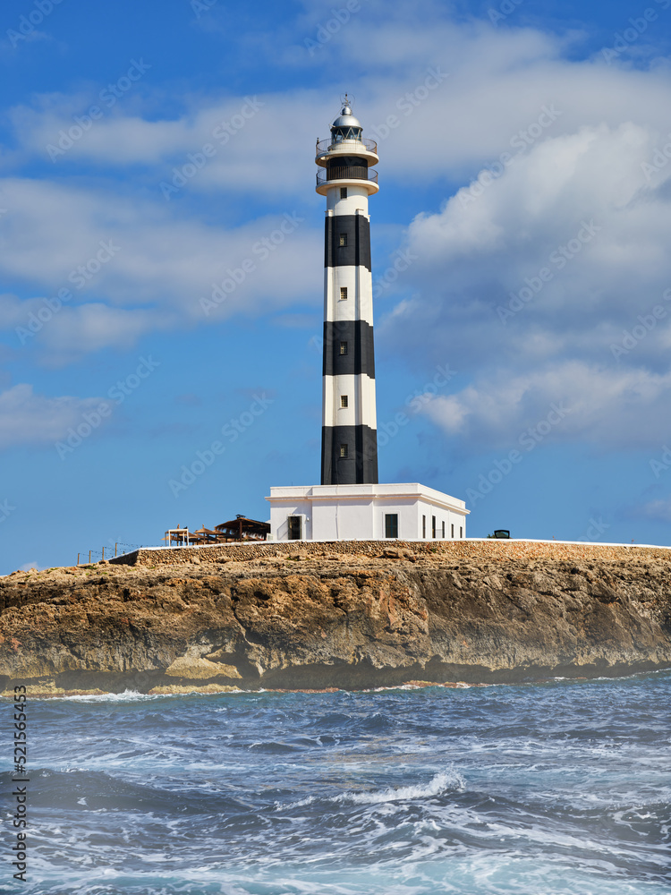 View from the sea of the black and white striped lighthouse on the coast of the island of Menorca, Spain