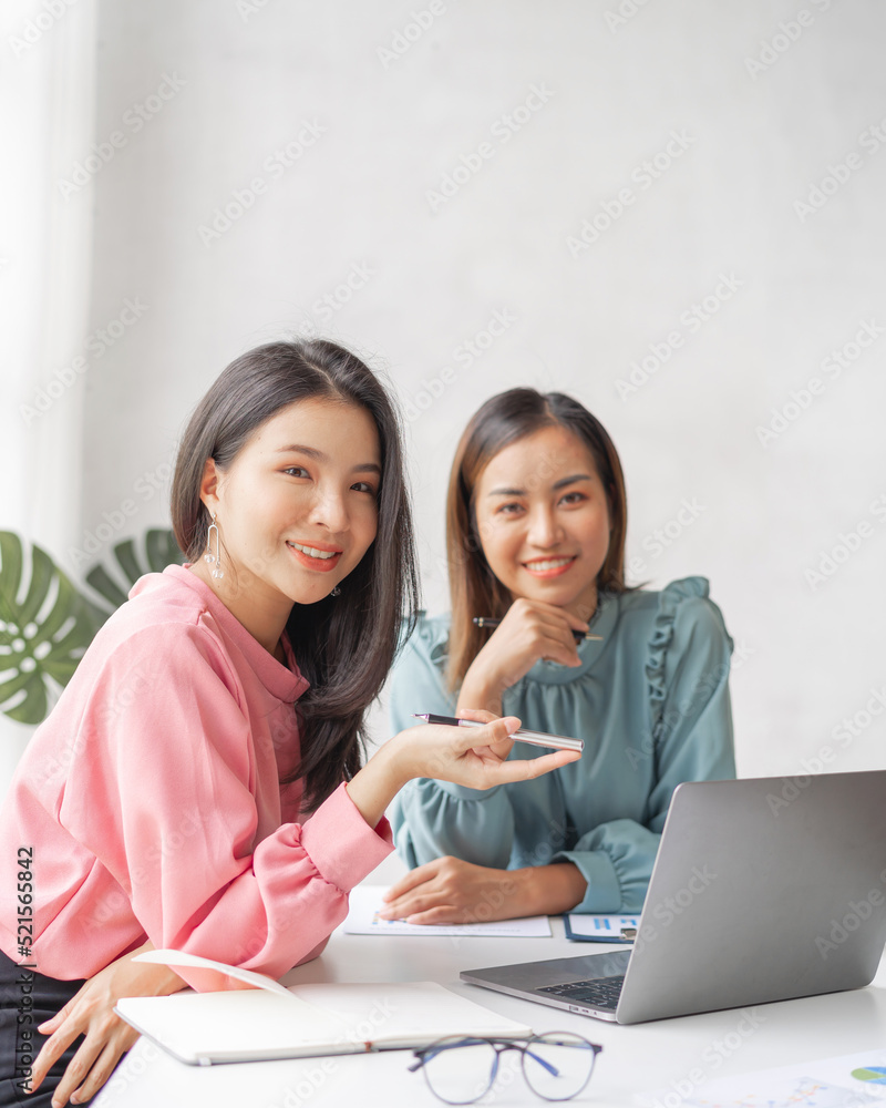 Two Young charming Asian businesswoman discussing and analyze planning and financial statistics when sitting at desk in workplace. Looking camera. Two Young charming Asian businesswoman discussing and analyze planning and financial statistics when sitting at desk in workplace. Looking camera.