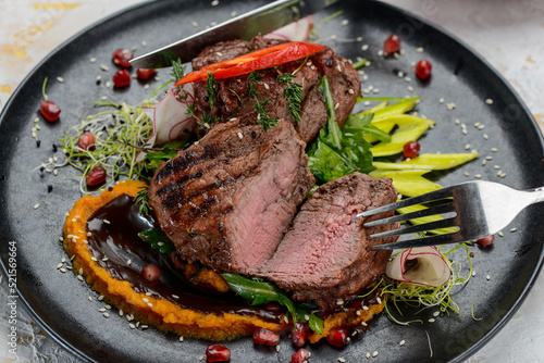 steak meat grilled on a black plate with salad is cut with utensils in female hands macro photo
