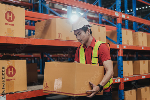 Warehouse Worker holding Box Product in Logistic center. Asian worker wearing hard hat and safety vests working about shipment in storehouse, Working in Distribution Center.