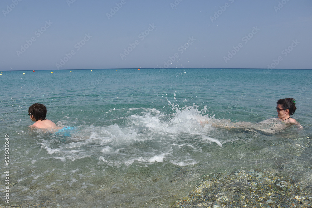 40 Years old Mom play with son in the sea. Cheerful child splashing and enjoy in water with his mother 40 Years old Mom play with son in the sea. Cheerful child splashing and enjoy in water with his mother