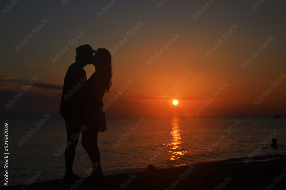 Romantic couple kissing on the beach with a beautiful sunset in background. Happy couple on summer vacation hugging and kissing at sunset