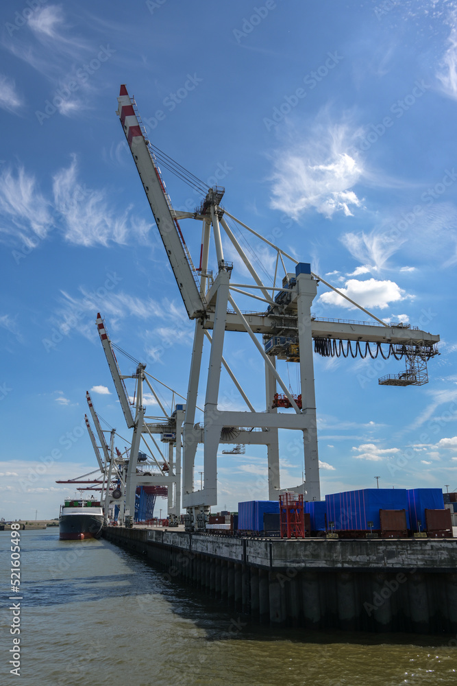 Cranes at a terminal in the cargo port of Hamburg against a blue sky with cirrus clouds, concept for transport, shipping and logistics, copy space Cranes at a terminal in the cargo port of Hamburg against a blue sky with cirrus clouds, concept for transport, shipping and logistics, copy space