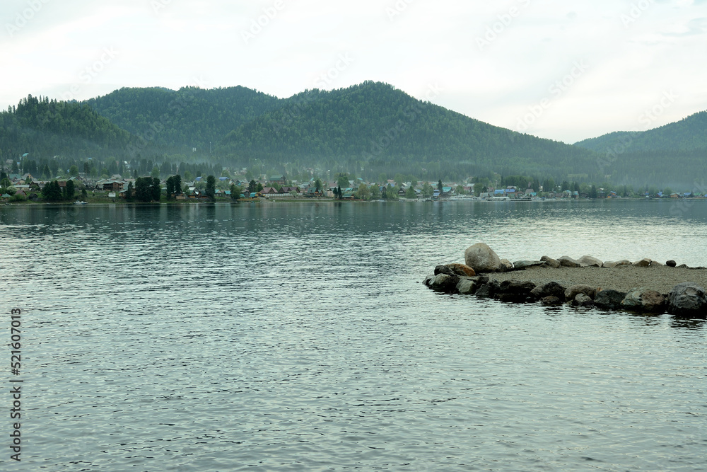 Obraz premium The ledge of the rocky shore overlooks the lake lying surrounded by high mountains overgrown with coniferous forest.