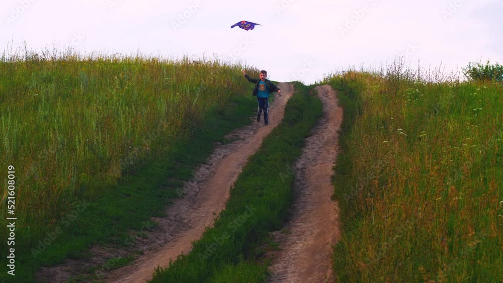 joyful caucasian boy 7-8 years old on a summer day runs along the road in the countryside holding a kite in his hands. Real kids. The child enjoys summer vacation runs along the road. joyful caucasian boy 7-8 years old on a summer day runs along the road in the countryside holding a kite in his hands. Real kids. The child enjoys summer vacation runs along the road.