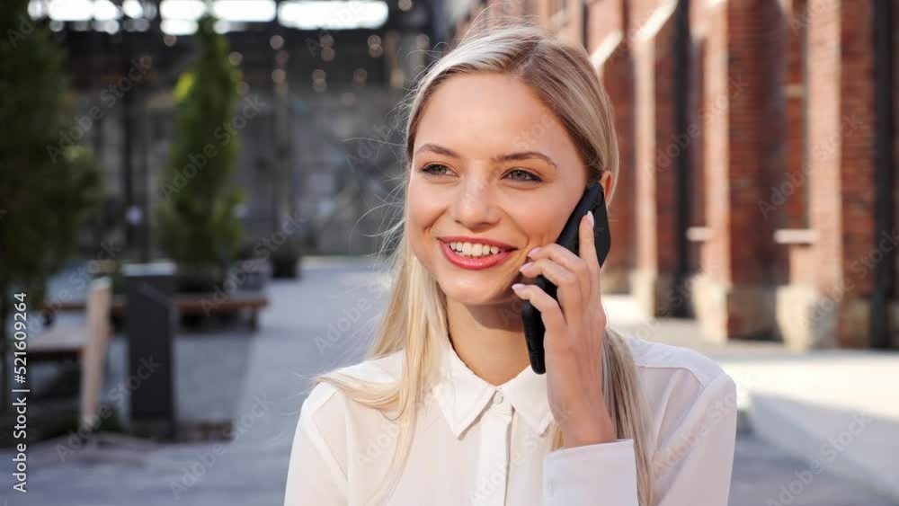 Smiling contented blonde woman talking on mobile phone with friends rejoicing smiling laughing white teeth, outdoors closeup. Girl student makes online order on smartphone outside, satisfied customer. Smiling contented blonde woman talking on mobile phone with friends rejoicing smiling laughing white teeth, outdoors closeup. Girl student makes online order on smartphone outside, satisfied customer.