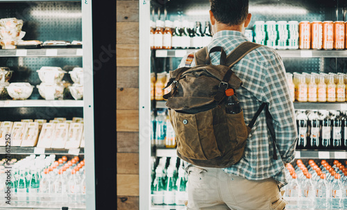 Traveler backpack man in front of a drinks and food window store. People and travel lifestyle buying some drinks and sandwiches before start the trip. Concept of automatic machine shop station