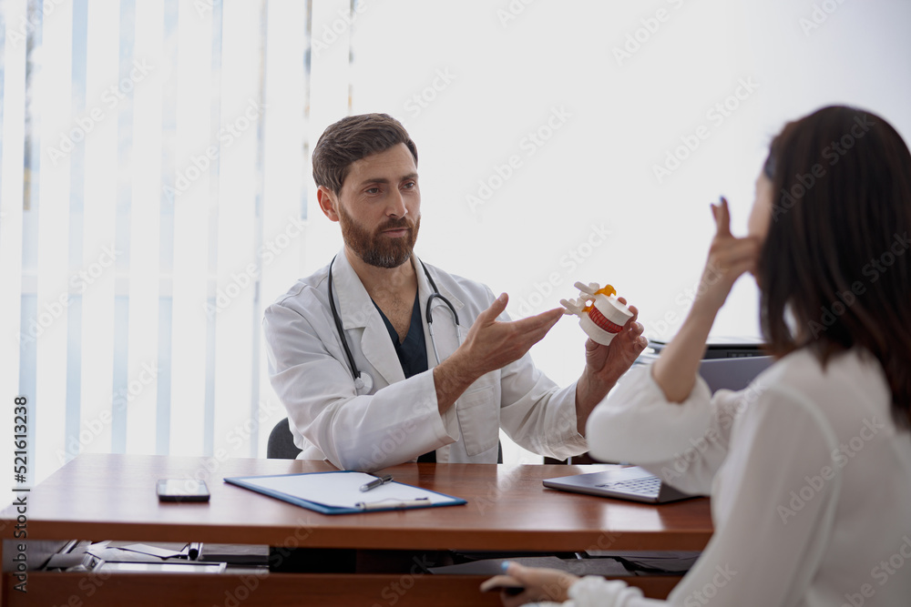 Male professional doctor consults patient and shows the model of several spines in modern clinic Male professional doctor consults patient and shows the model of several spines in modern clinic