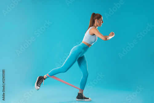 Fototapeta Naklejka Na Ścianę i Meble -  Trainer girl in blue clothes working the buttocks with an elastic band on a blue background.