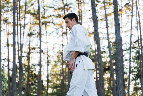 A young guy doing karate training and meditation in the forest during the day