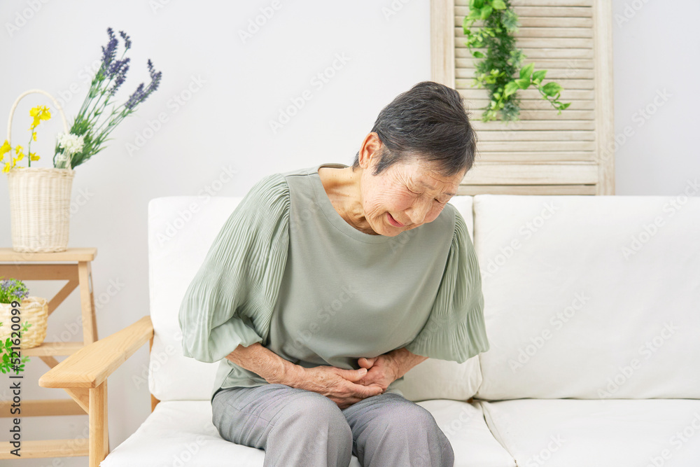 自宅で腹痛を感じるシニア女性 自宅で腹痛を感じるシニア女性
