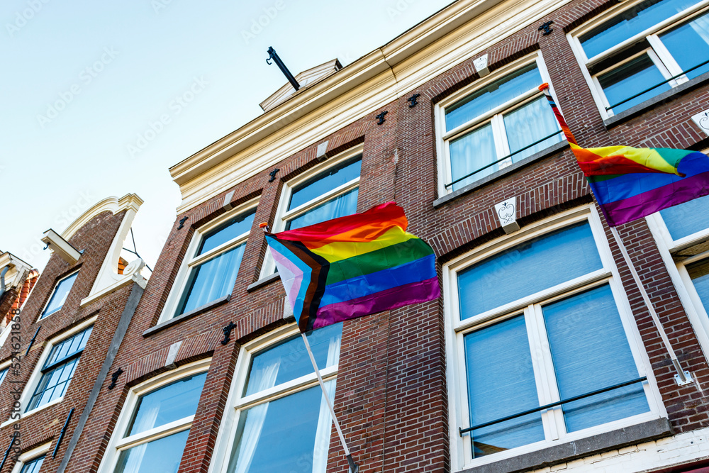 Old Dutch canal houses in Amsterdam with a Progress Pride Flag on their facades during Gay Pride Amsterdam, The Netherlands, Europe