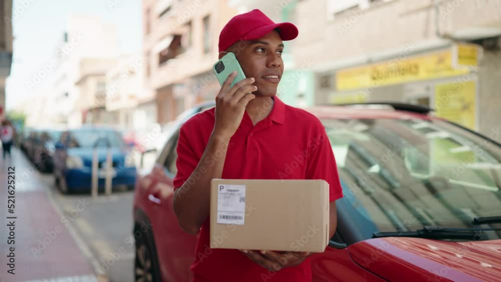 Young latin man delivery worker holding package talking on smartphone at street Young latin man delivery worker holding package talking on smartphone at street