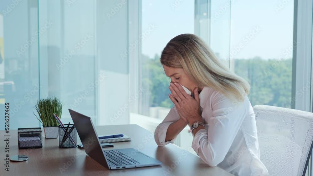 Tired office female worker sneezing from allergy blowing nose using napkins working on laptop computer in the company. Overwhelmed young businesswoman working on pc suffering from coughing infectious. Tired office female worker sneezing from allergy blowing nose using napkins working on laptop computer in the company. Overwhelmed young businesswoman working on pc suffering from coughing infectious.