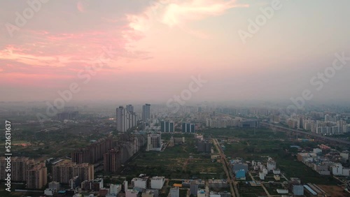aerial drone shot flying towards skyscrapers surrounding green feilds and parks under the pink orange sky of dusk dawn showing monsoon in gurgaon, delhi kolkata in India photo