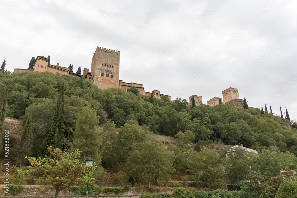 View at the Alhambra citadel on top, from Paseo de los Tristes, walk of the sad (The Promenade of the Sad), classic buildings and woods around, Granada, Spain