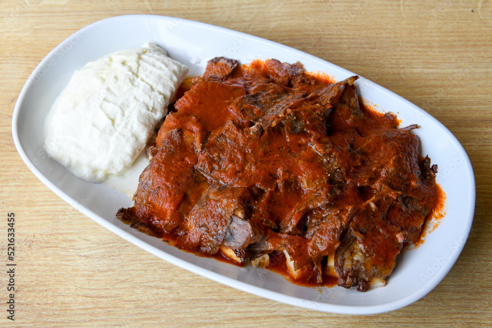 Turkish and Arabic Traditional Ramadan doner kebab with tasty tomato sauce and rice or turkish pilav in white plate on wood table background. ( , Iskender, ekmek arasi pilav ustu doner, doner durum ) Turkish and Arabic Traditional Ramadan doner kebab with tasty tomato sauce and rice or turkish pilav in white plate on wood table background. ( , Iskender, ekmek arasi pilav ustu doner, doner durum )