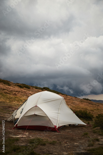 White tent in meadow with view of Mountain range with rain clouds in front. Carpathian Mountain, Ukraine. Walking and hiking trails in Marmaros ridge. Camping in Carpathian Mountains in autumn