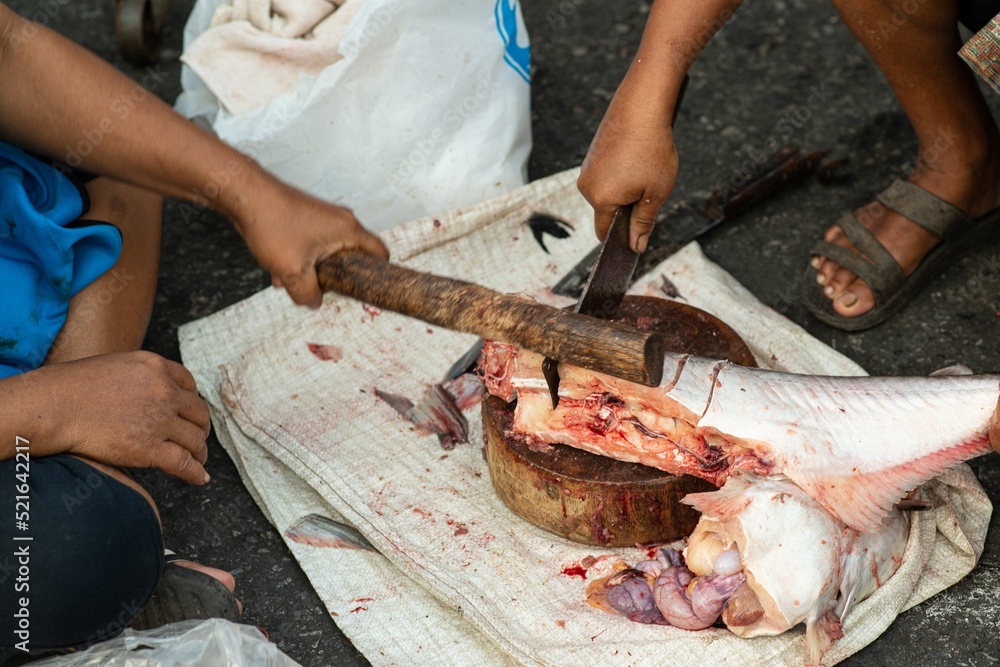 A merchant uses a knife to cut the fish into pieces for sale. In one of the morning markets in Thailand.. A merchant uses a knife to cut the fish into pieces for sale. In one of the morning markets in Thailand..