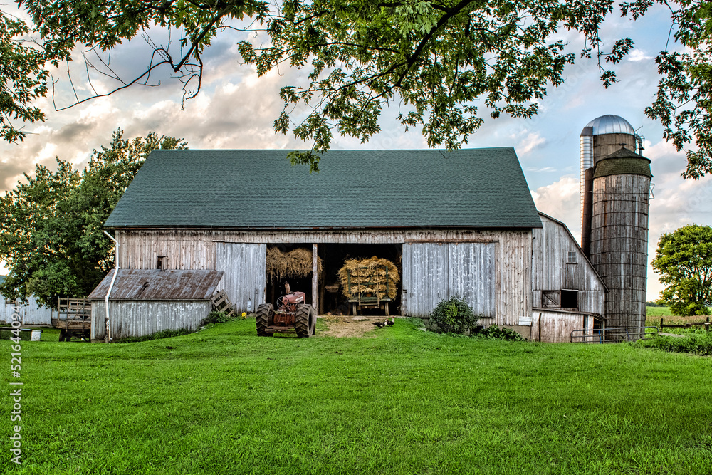 barn with grain shocks on farm wagon and tractor.