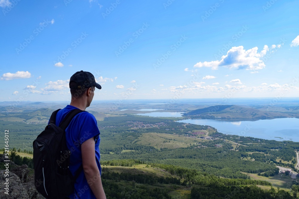 Fototapeta premium A man with a backpack stands on a mountain and looks at the lakes on a summer day