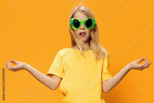 a beautiful girl in funny green sunglasses stands in bright clothes on an orange background spreading her arms to the sides