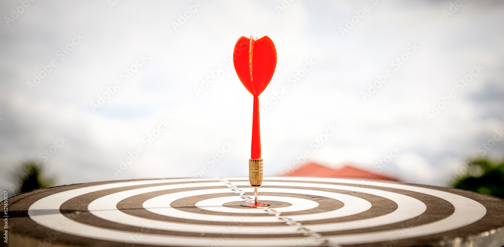 Close up shot red darts arrows in the target of dartboard center on dark blue sky background. Business target or goal success and winner concept. Close up shot red darts arrows in the target of dartboard center on dark blue sky background. Business target or goal success and winner concept.