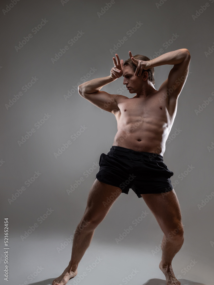 young muscular man in an expressive pose, artistic pose of the hero with outstretched arms. Beautiful muscles. extraordinary athletic body. Portrait on a gray background